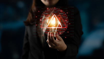 A businesswoman holds a glowing warning symbol against a digital backdrop filled with binary code, emphasizing the importance of cybersecurity and risk awareness in today technical landscape. Gantry
