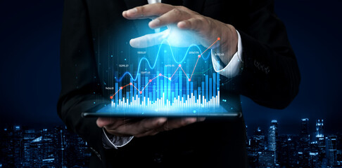 A businessman in a formal suit showcases a futuristic digital data visualization on a tablet, emphasizing analytics and modern business strategies against a nighttime city backdrop. Scalp