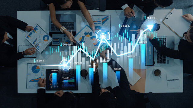 Aerial view of a busy business meeting with professionals analyzing growth charts and data on digital devices and printed reports, showcasing teamwork and strategy. Scalp