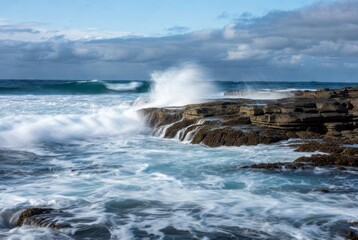 Ocean Waves Crashing on Rocky Shoreline: A captivating view capturing the raw power of the ocean as waves relentlessly crash against a rugged, rocky shoreline.
