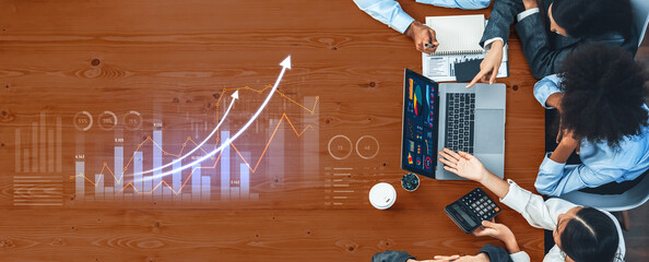 A diverse business team collaborates during a meeting, analyzing financial data with graphs and charts displayed on a laptop at a modern office table. Scalp