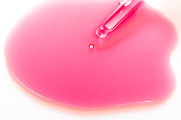 Pipette releasing drop of pink serum or chemical reagent. Concept of cosmetic formulation, laboratory and scientific analysis.