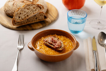 Autumn pumpkin soup served with toasted bread crouton and sausage. Rustic hot comfort food on a set table.