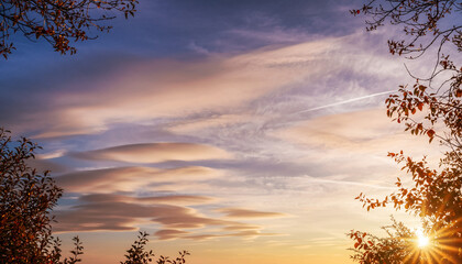 Colorful sunset sky over a mountain forest landscape with silhouettes of trees and light breaking through the clouds at dusk