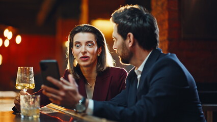 Elegant pair flirting bar counter staring smartphone together at evening closeup