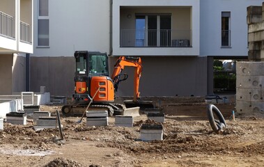 A shovel and a compact excavator on dirt area in front of new residential building under...