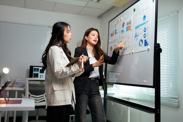 Businesswomen analyzing data charts on office whiteboard