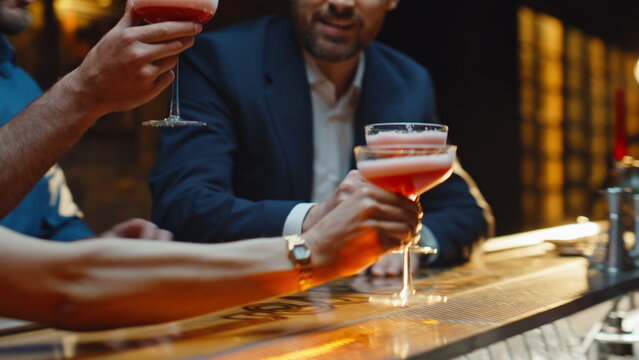 Hands taking cosmopolitan cocktails from bar closeup. Friends toasting glasses