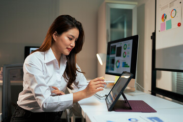 Woman analyzing data on tablet and computer in office