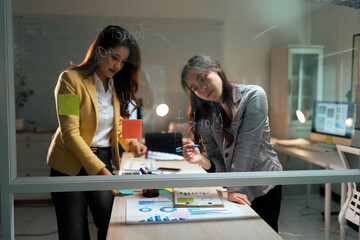 Businesswomen planning strategy on glass whiteboard at night office