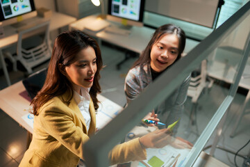 Asian businesswomen collaborating on glass board in modern office