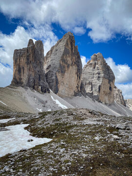 Close view of Tre Cime di Lavaredo in Italy, the three Dolomite towers rising above pale limestone scree and late snow against blue sky with clouds