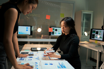 Businesswomen analyzing market data charts during late night meeting