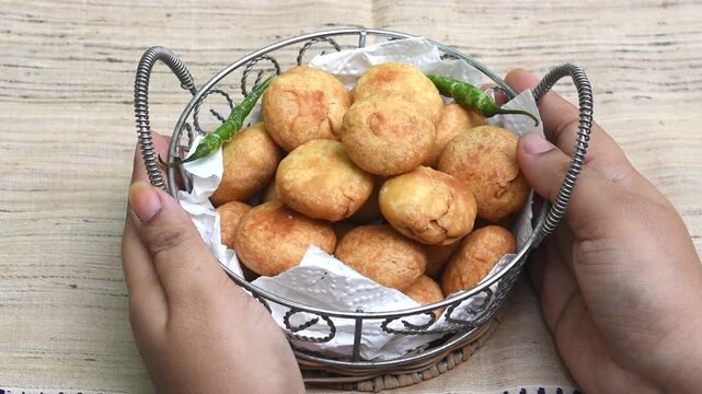 Kachori with fried green chilli in a basket. hand holding the basket. 