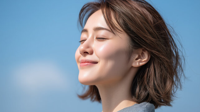 Radiant woman with glowing skin and softly shut eyes enjoys serene moment outdoors under clear blue sky, expressing peaceful happiness and natural beauty