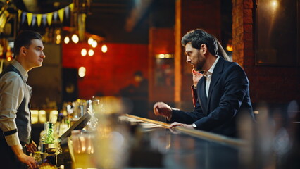 Couple entering evening bar. Man talking bartender ordering drinks at counter