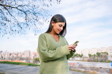 Young woman smiling while texting on phone in city park