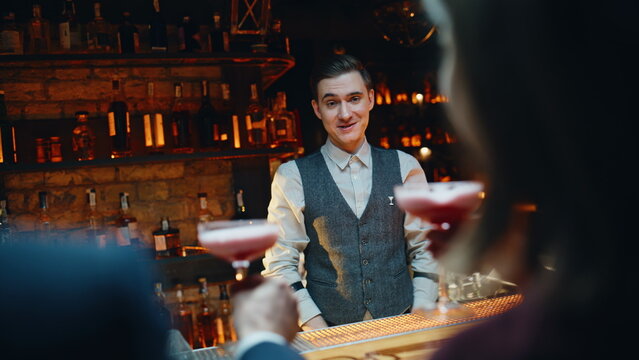 Bar guests appreciating cocktails counter back view. Mixologist feeling grateful