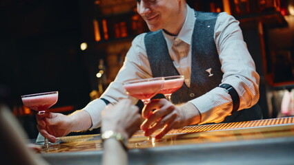 Cheerful barman putting cocktails on counter inside. Bar worker giving beverages