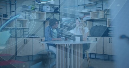 Reviewing docs, pair wearing business attire working at round table with laptop, blue overlay