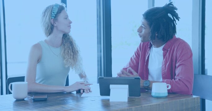Discussing woman in sleeveless top and man in red shirt reviewing tablet papers at cafe