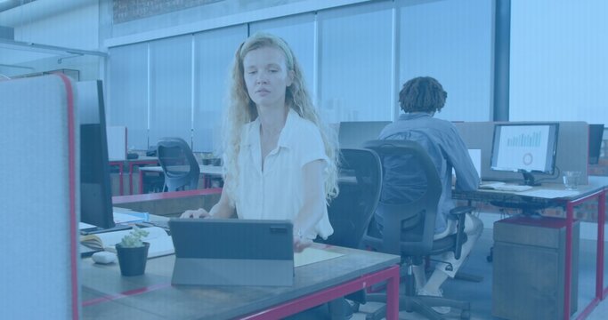 Woman with long hair tapping tablet with keyboard cover at office desk, wearing light blouse