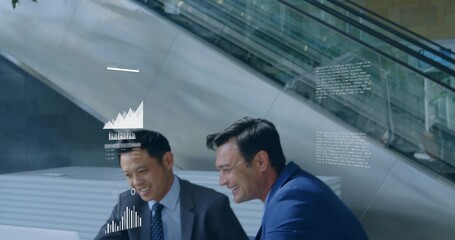 Leaning two men in business suits examining laptop at corporate atrium, with holographic charts
