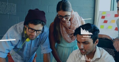 Collaborating team wearing beanie and scarf reviewing laptop in modern office, with sticky notes