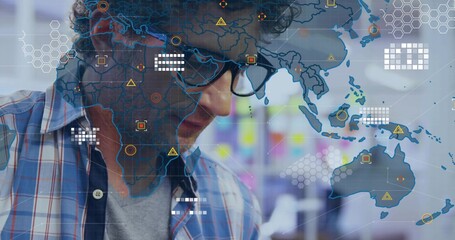 Mature man black-framed glasses blue plaid shirt gray tee studying data with map overlay at office