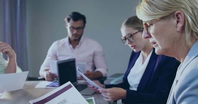 Reading woman in light blazer and glasses studying papers at meeting table with tablet, copy space