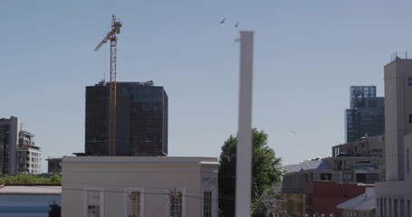 Framing dark glass mid-rise tower rising from street-level, with yellow crane, low-rise roofs