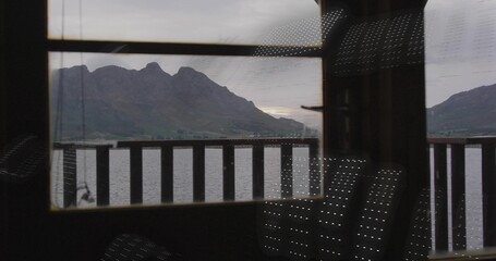 Fototapeta premium Framing jagged mountain ridge and calm lake through window in dim cabin, with railing reflections