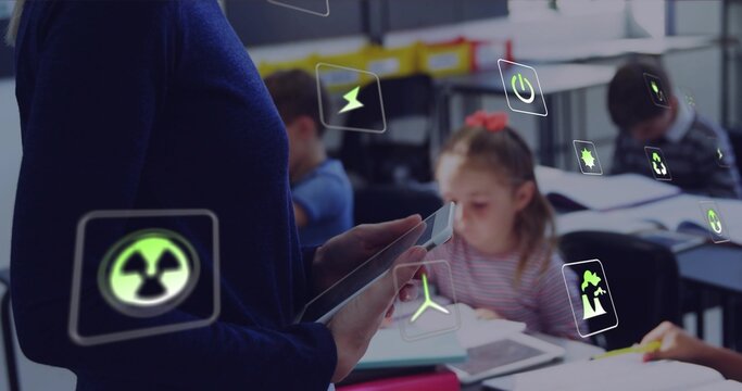 Showing teacher holding tablet in classroom in blue top, students using notes, AR icons, copy space