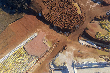 Abstract drone shot capturing the vibrant contrasting colors of an open-pit mine. The piles of bright yellow minerals, red clay, and white earth create a unique industrial landscape texture.