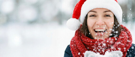 Joyful Celebration in Winter Wonderland: A person radiates festive cheer, wearing a Santa hat and scarf amidst a flurry of snowflakes, Christmas banner, blank space