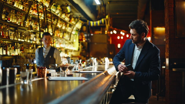 Rich businessman resting bar counter choosing menu options in evening light - Powered by Adobe