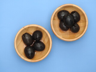 Set of black olives in wooden elements on a blue background