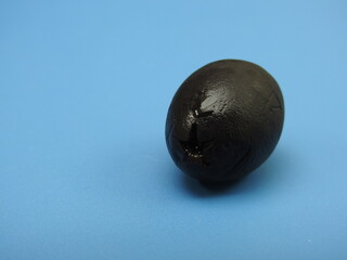 A solitary black olive placed on a blue background