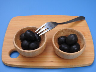 Set of black olives in wooden elements on a blue background