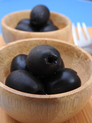 Set of black olives in wooden elements on a blue background