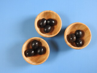 Set of black olives in wooden elements on a blue background