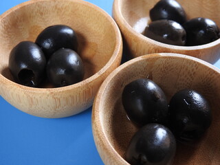Set of black olives in wooden elements on a blue background