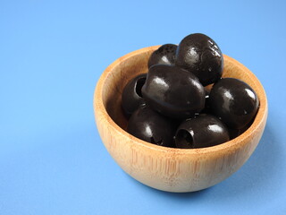 Set of black olives in wooden elements on a blue background