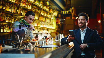 Laughing gentleman relaxing counter requesting strong beverage inside dark pub