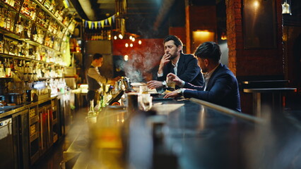 Drunk bar visitors resting counter holding glasses smoking under warm lighting