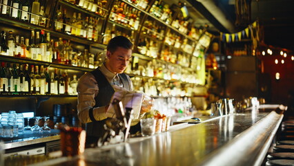 Evening staff polishing bar table in moody lounge. Waiter tidying workspace