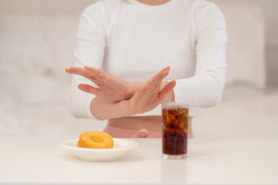 Woman on diet refusing soda and donut with hand gesture, symbolizing healthy lifestyle, sugar reduction, calorie control, and commitment to clean eating for weight loss.