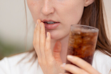 Young woman with toothache holding a glass of cold soda, showing discomfort and dental sensitivity....