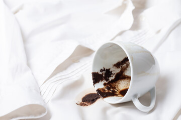 a white cup with the remains of coffee, spilled, lies on a white shirt, there are no people, a soft focus,