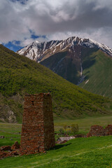 Old stone tower beneath steep green slope and snowy summit